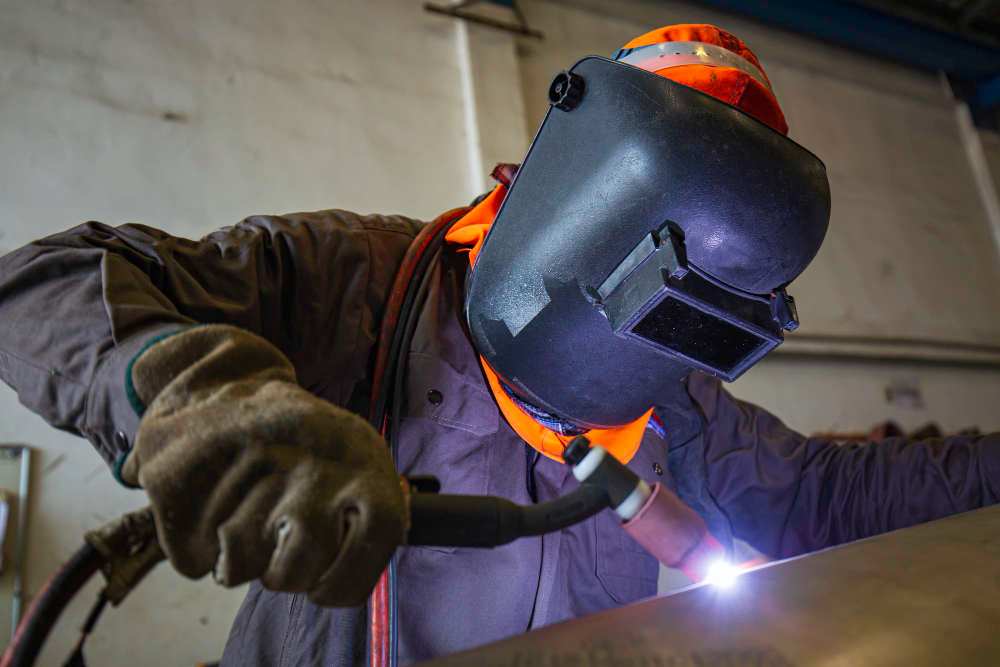 Profissional em uma oficina de serralheria usando os equipamentos de proteção individual como luvas e capacete de solda