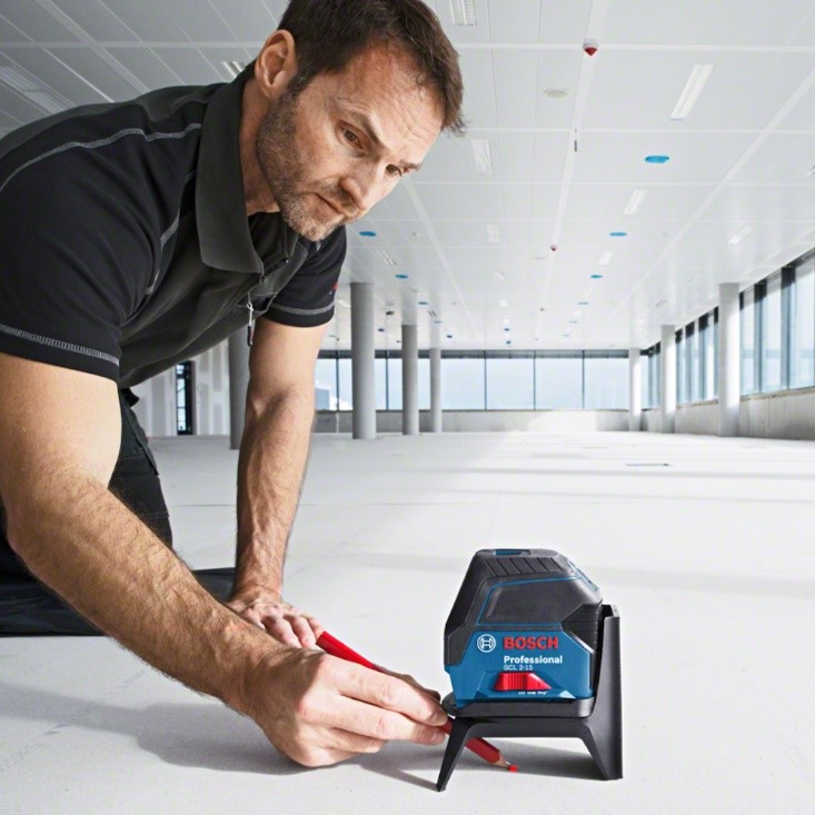 Homem utiliza o nível a laser bosch gcl 2-15 e usa um lápis para fazer marcação no piso.